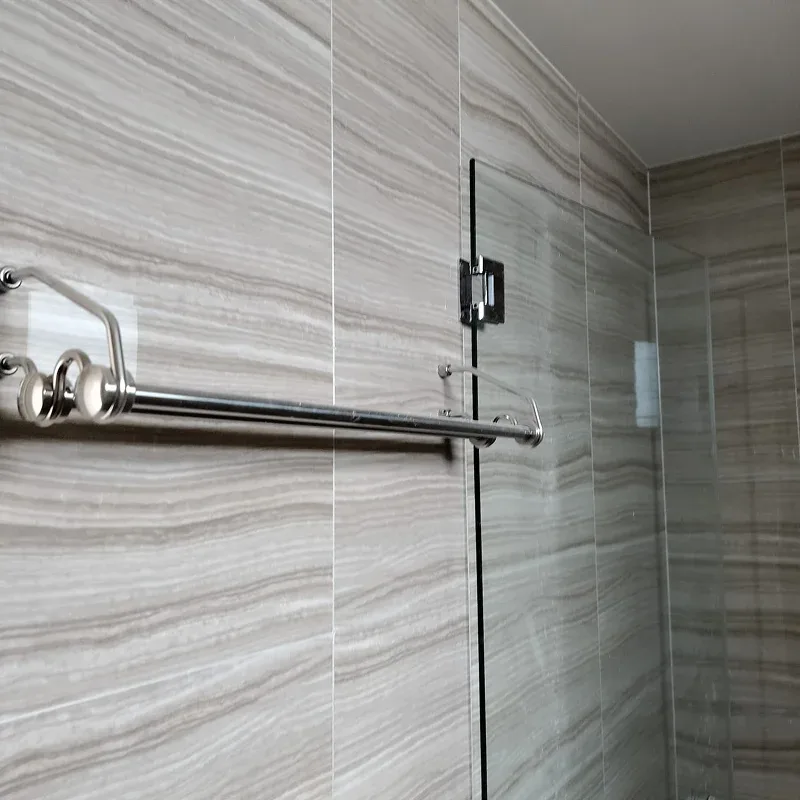 A stainless steel towel rack mounted on a grey marble-patterned tiled bathroom wall next to a glass shower door. Experienced tiling contractor installing premium floor tiles in Singapore