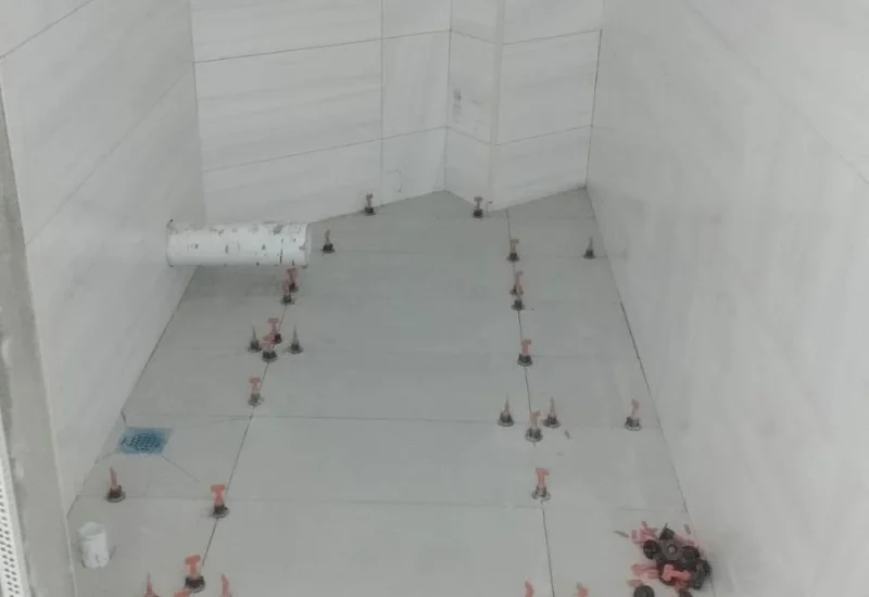 Ongoing tile installation on a bathroom floor using red tile leveling clips and spacers.