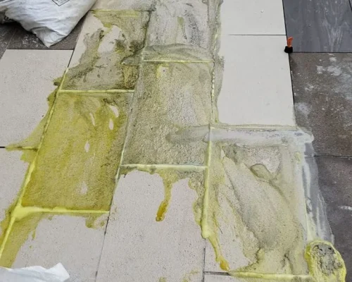 Outdoor tiling installation with yellowish liquid adhesive mortar spread across tiled surface gaps.