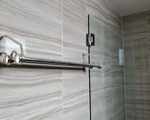 A stainless steel towel rack mounted on a grey marble-patterned tiled bathroom wall next to a glass shower door. Experienced tiling contractor installing premium floor tiles in Singapore