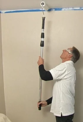 A painter wearing safety glasses using a paint roller with an extension pole to paint a white ceiling with painter's tape along the edge. Expert demolition and hacking works for renovation projects in Singapore